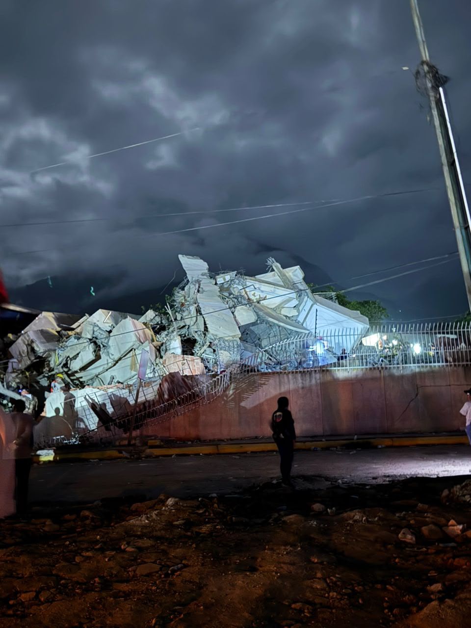 Collapsed concrete structure at night, rescue workers visible